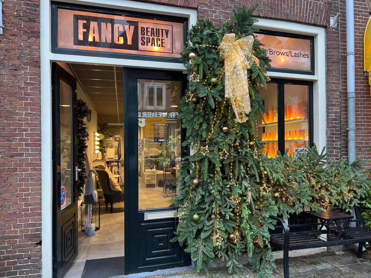De verlichte gevel van Fancy Beauty Space met kerstgroen en een gouden strik